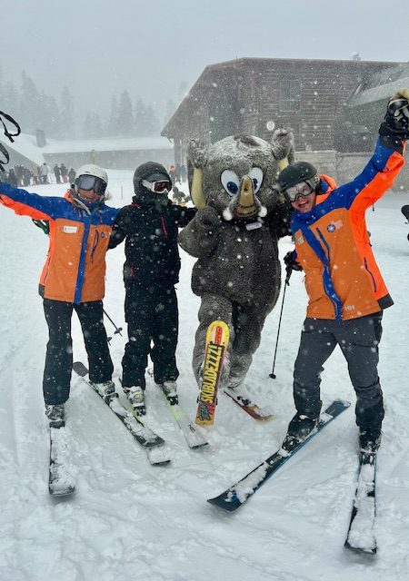 Explore our programs.winter sports Access Mammoth ski instructors and adaptive skier with Mammoth mascot in the snow