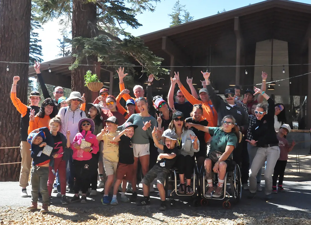 Group of families and participants, including children and wheelchair users, celebrating together at an outdoor adaptive family camp.