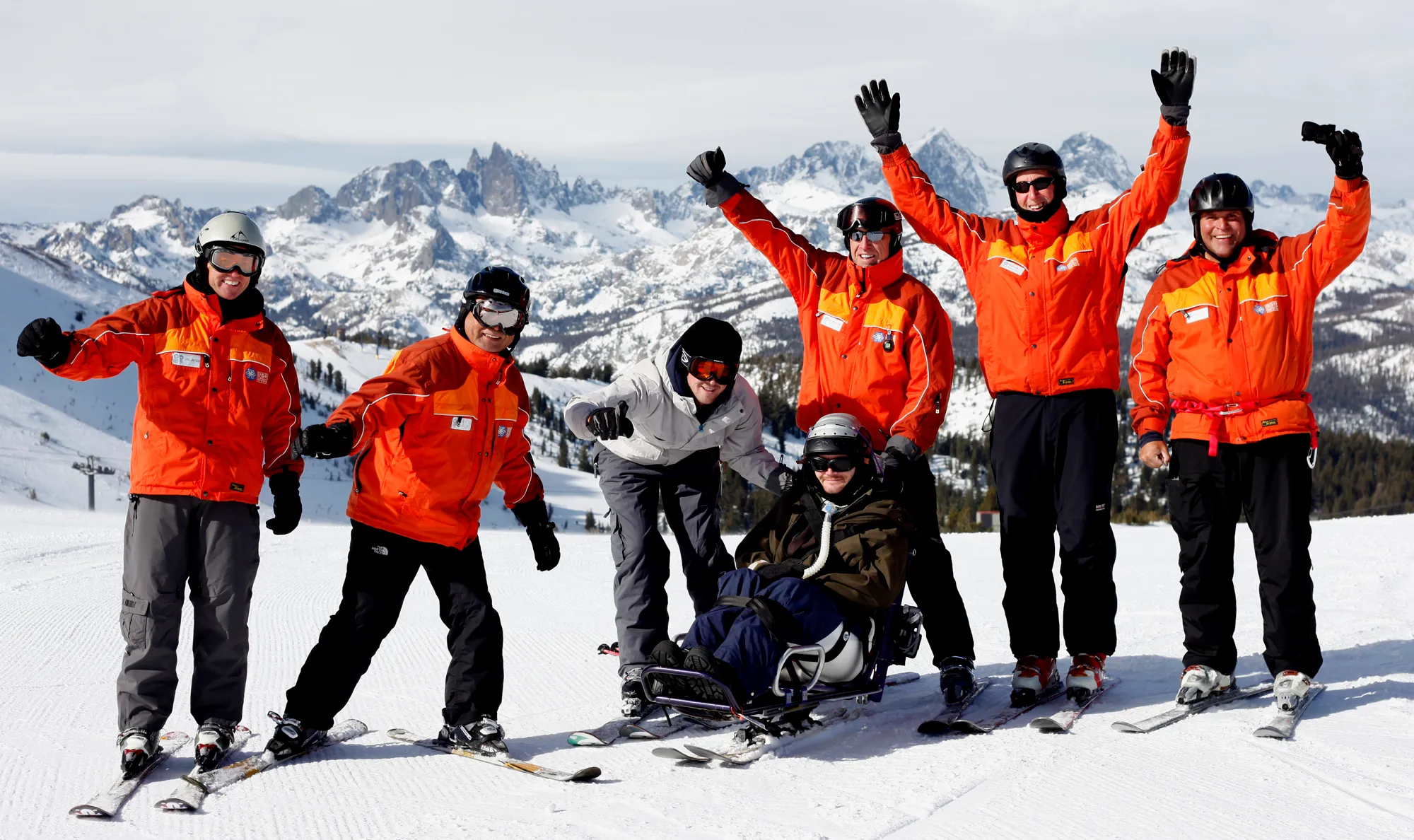 Group of Access Mammoth volunteer instructors posing for a photo with an adaptive skier in front of a mountain landscape