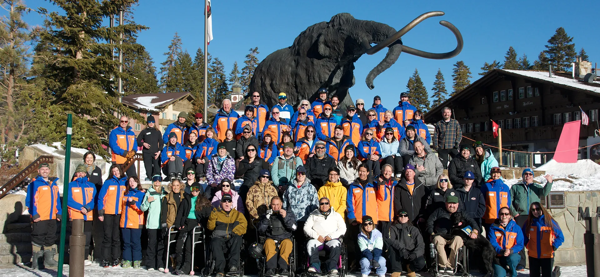 Large group of adaptive sports participants, veterans, and volunteers posing together at Mammoth Mountain with the iconic woolly mammoth statue.