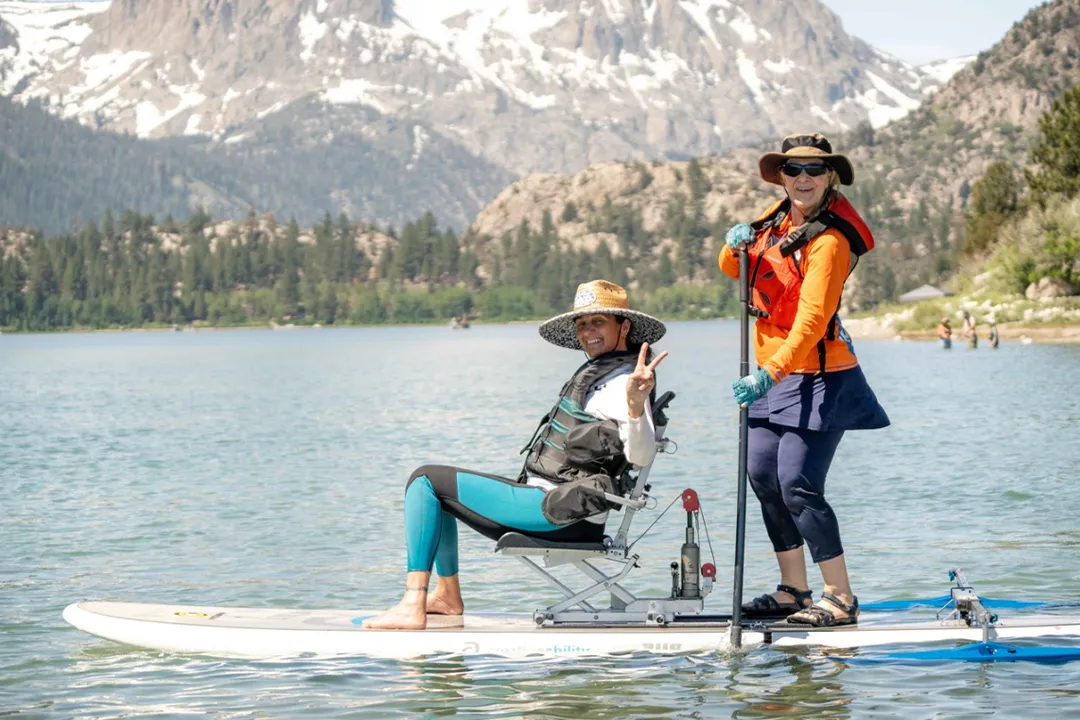 An access mammoth instructor and adaptive athlete on a paddle board smiling at the camera during one of our summer programs