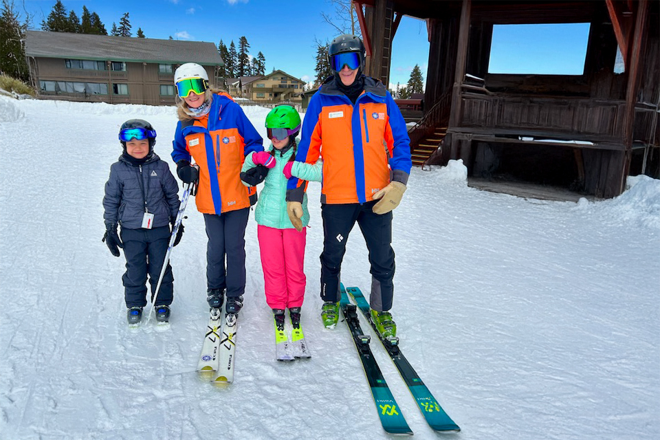 Ski instructors with children learning to ski on a snowy slope during an adaptive ski lesson.